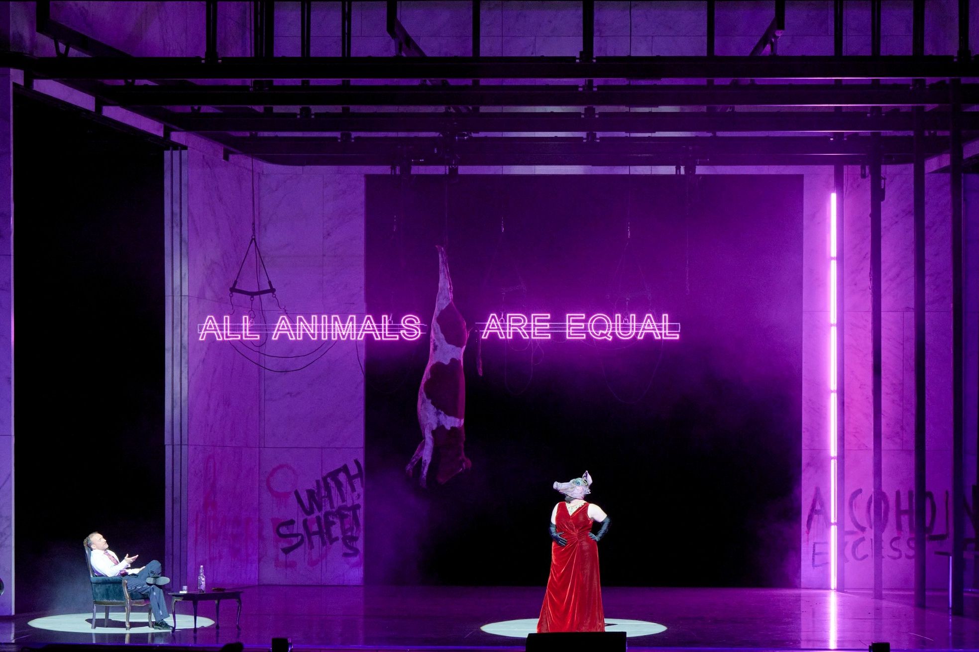  Eine Figur mit Schweinemaske steht in rotem Gewand im Zentrum einer lila beleuchteten Bühne, hinter ihr leuchtet der Satz „ALL ANIMALS ARE EQUAL“.