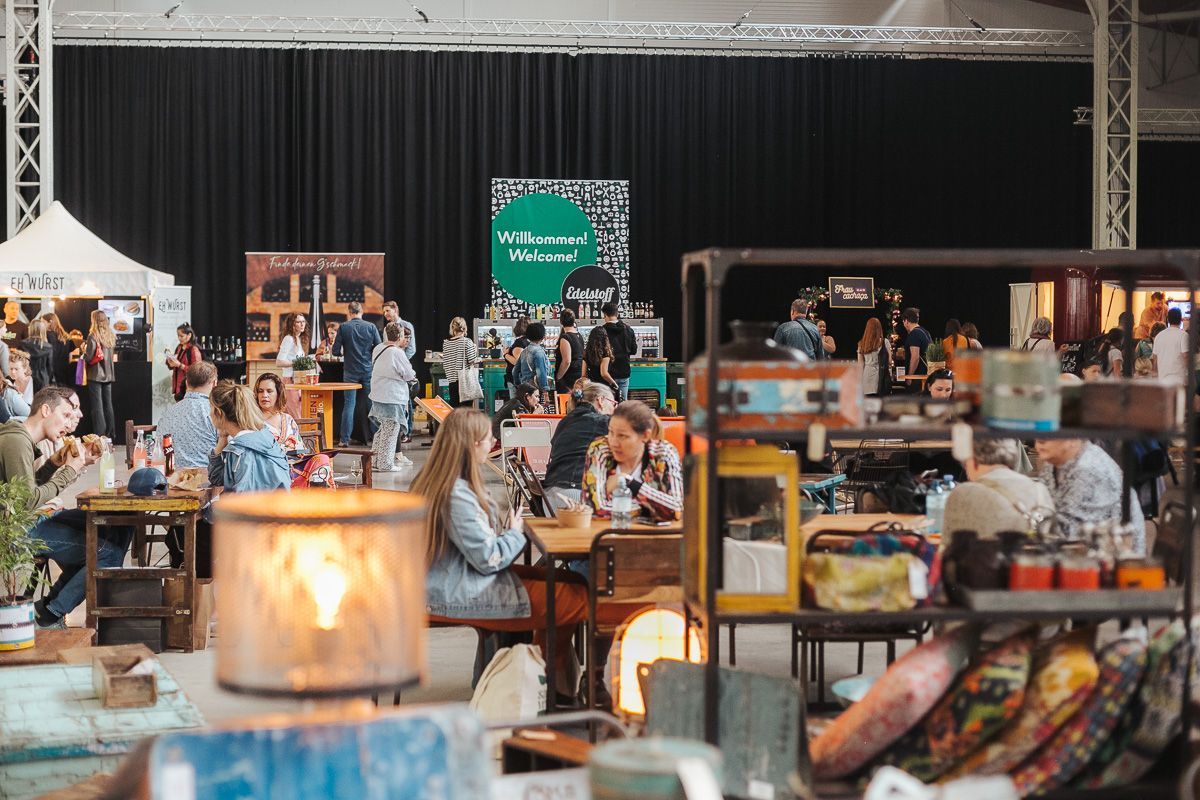The photo shows a scene from the Edelstoff design market: various stands with special design products, visitors strolling around, sitting comfortably and eating something