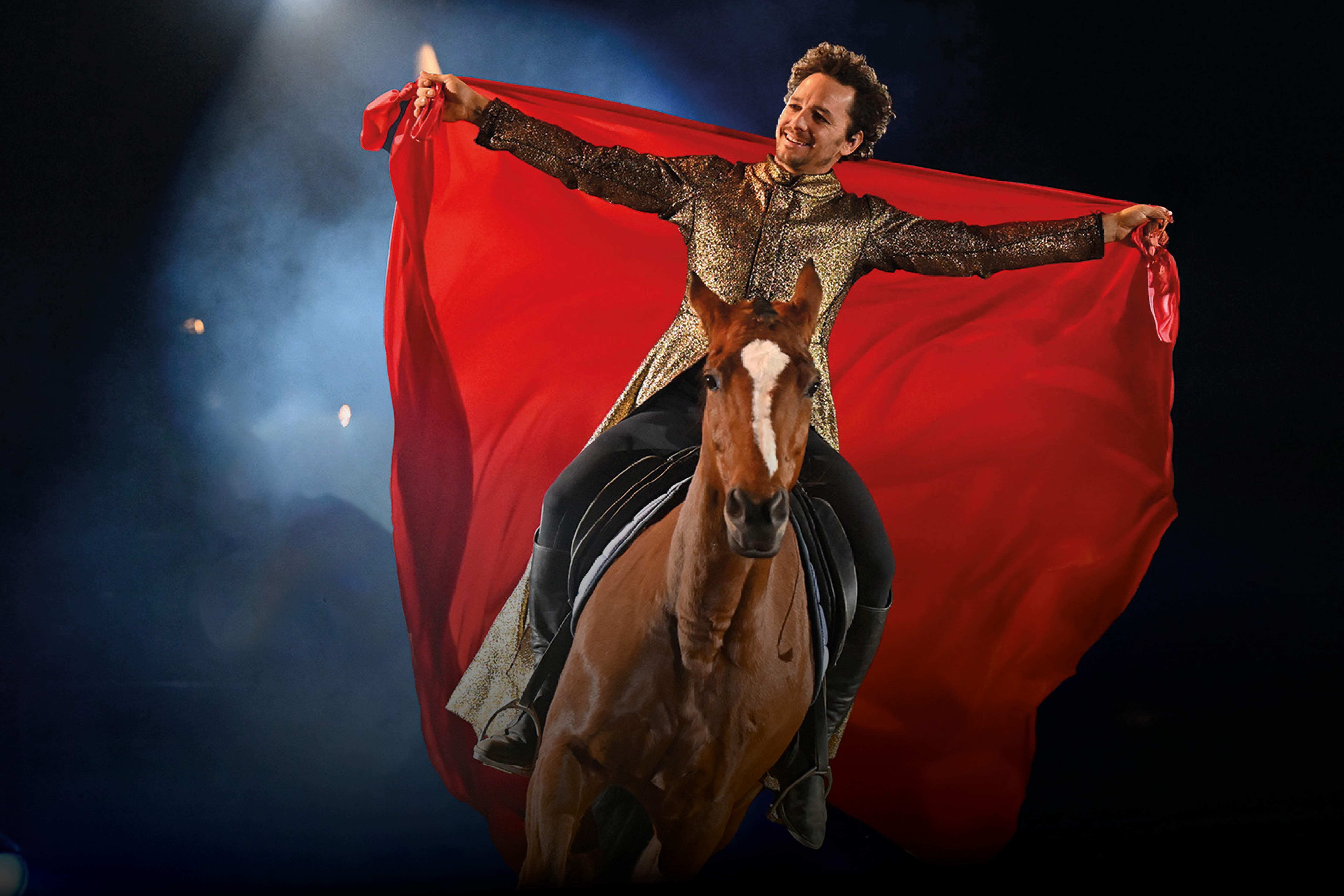 Das Foto zeigt einen Reiter in goldschwarzem Kostüm auf einem braunen Pferd. Der Reiter reitet mit ausgestreckten Armen und hält ein rotes Tuch in Händen