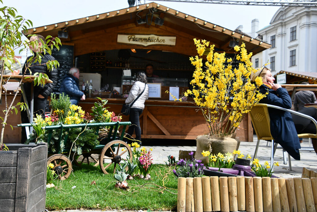 Das Foto zeigt eine Hütte am Ostermarkt am Hof, davor österliche Dekoration und Frühlingsblumen