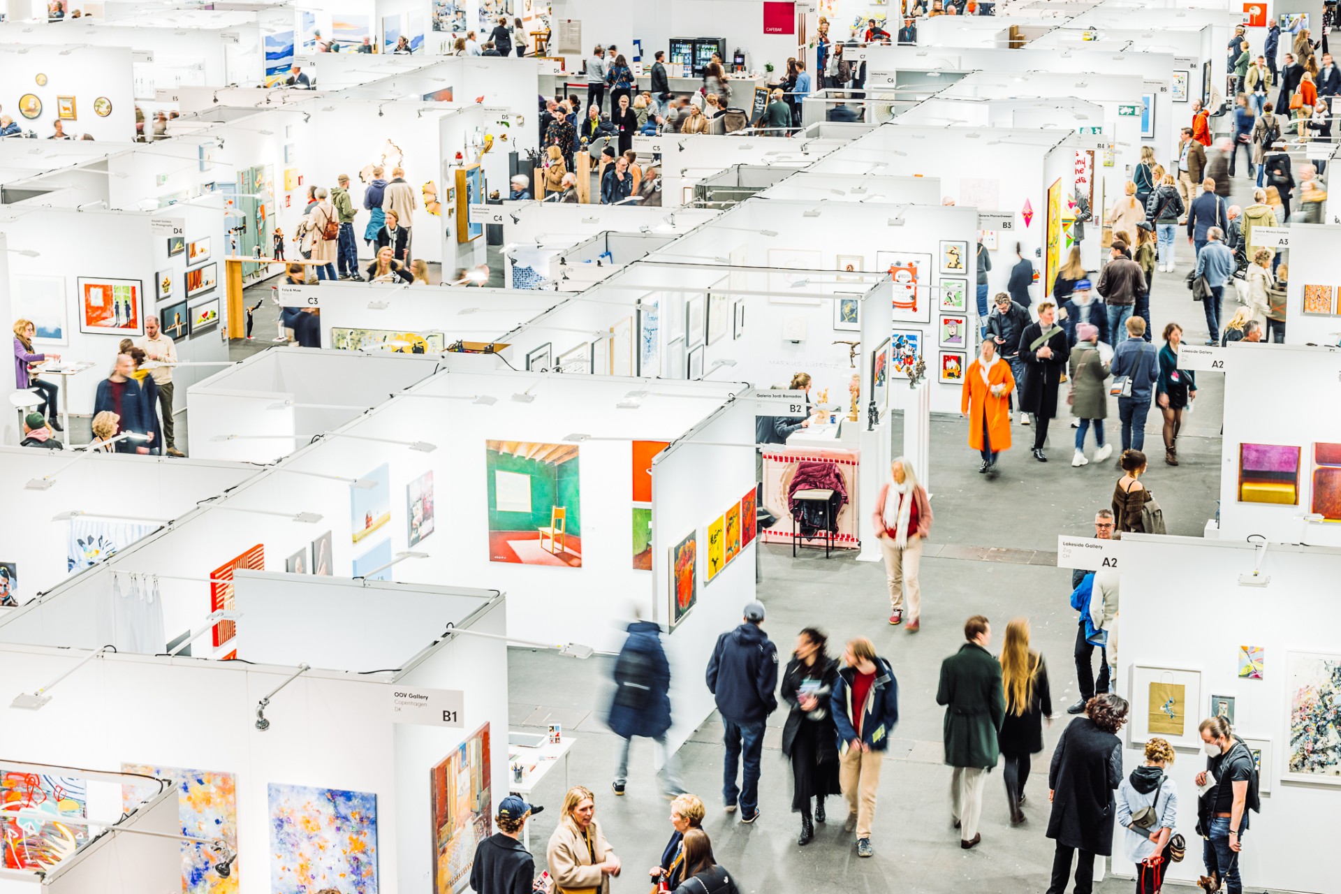 The photo offers a view of the Affordable Art Fair 2025 from above, showing white booths with artworks, paintings, pictures and fair visitors strolling and exchanging ideas.